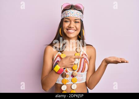 Belle femme hispanique portant le style bohème et hippie stupéfait et souriant à l'appareil photo tout en présentant avec la main et pointant avec le doigt. Banque D'Images