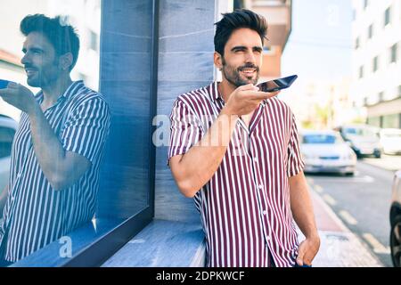 Jeune beau hispanique homme avec la barbe souriant envoi plein air heureux message vocal sur le téléphone Banque D'Images