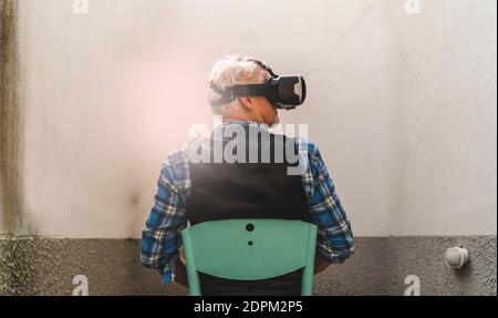 Vue arrière de l'homme senior regardant à travers le simulateur de réalité virtuelle tout en étant assis sur la chaise