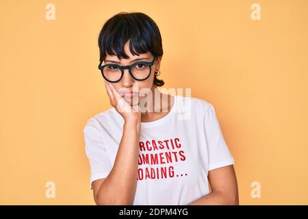 Belle femme brunettte portant des commentaires sarcastique chargement t-shirt penser en train de regarder fatigué et s'ennuyer avec des problèmes de dépression avec les bras croisés. Banque D'Images