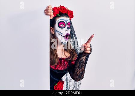 Jeune femme portant le jour de la custome mort tenant blanc bannière vide pointant avec le doigt surpris devant, bouche ouverte expression stupéfait, quelque chose o Banque D'Images