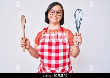 Brunette femme avec le syndrome de Down cuisson à l'aide d'un fouet boulanger et d'une cuillère souriant avec un sourire heureux et frais sur le visage. Montrant les dents. Banque D'Images