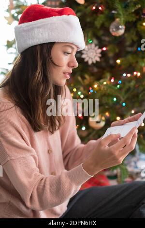 Jolie carte de noël pour femme d'âge universitaire lisant près de l'arbre de Noël Banque D'Images