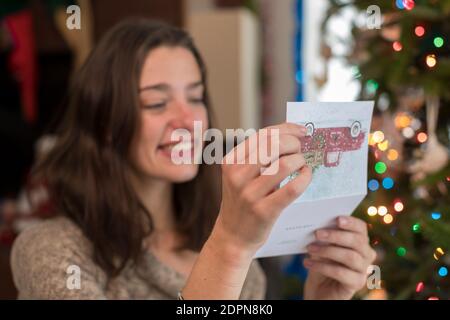 Femme d'âge universitaire lisant la carte de noël par arbre de noël Banque D'Images