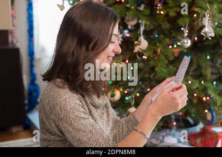 Femme d'âge universitaire regardant la carte de noël par arbre de noël Banque D'Images