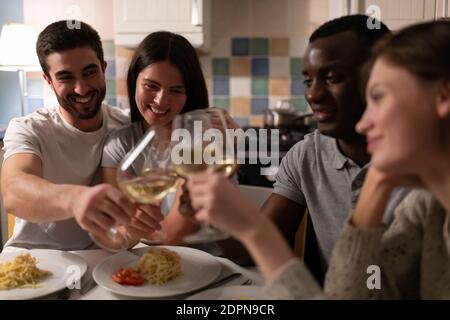 Divers jeunes hommes embrassant des amies et des verres de vin clinking en vous reposant pendant la fête à la maison dans la cuisine Banque D'Images