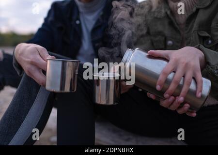 Gros plan une femme anonyme qui verse du thé chaud à la vapeur à partir de thermos des tasses en métal tout en se relaxant dans une nature paisible au crépuscule Banque D'Images