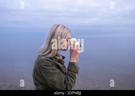 Vue latérale de la jolie culotte taille basse féminine dans une tenue décontractée prendre des photos de la nature tout en se tenant près du lac au coucher du soleil Banque D'Images