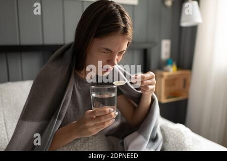 Jeune femme avec un verre d'eau douce s'accroupir après avoir pris sirop de toux amer tout en souffrant de la grippe au lit Banque D'Images