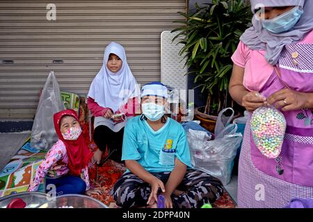 Les enfants musulmans portant le hijab traditionnel pour les filles et kufis ou taqiyah cap pour le garçon tout en aidant la mère dans la rue Sweet stall. Thaïlande Banque D'Images