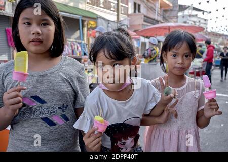 Enfants qui mangent des suces glacées à l'extérieur. 3 jeunes amis avec une fille tenant un poing plein d'argent et désireux de s'évader pour plus. Banque D'Images