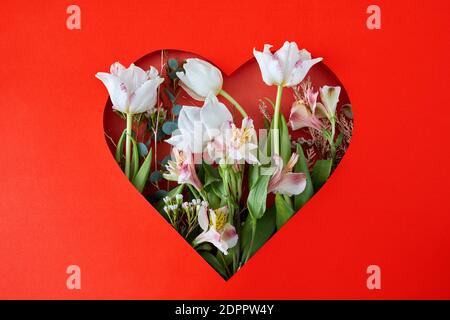 Trou en papier rouge en forme de coeur à travers lequel les tulipes et les feuilles sont visibles. Concept de bonne Saint Valentin Banque D'Images