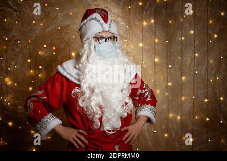 Le Père Noël pose dans un masque sur un fond de mur avec une guirlande montre différents gestes avec ses mains Banque D'Images