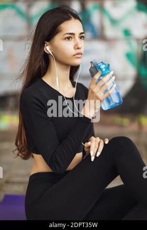 La jeune femme en noir SPORTSWEAR écoute de la musique et se repose après l'entraînement. Banque D'Images