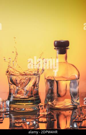 Glace tombant sur un verre de whisky et une bouteille de liqueur à base d'orange avec glaces. Concept whisky et boissons alcoolisées. Banque D'Images