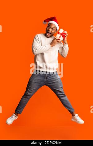 Homme noir émotif en chapeau de père noël sautant avec cadeau de noël boîte Banque D'Images
