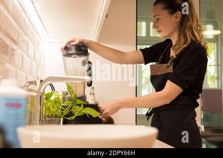 Jeune femme attrayante debout devant le blender dans sa cuisine, cuisant des repas végétariens frais pour la famille. Jeune femme blonde cuisine dans le TH Banque D'Images