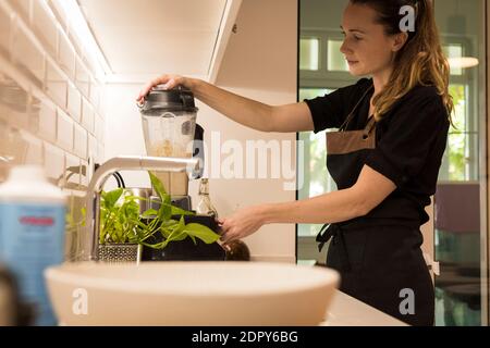 Jeune femme attrayante debout devant le blender dans sa cuisine, cuisant des repas végétariens frais pour la famille. Jeune femme blonde cuisine dans le TH Banque D'Images