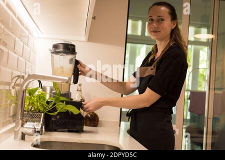 Jeune femme attrayante debout devant le blender dans sa cuisine, cuisant des repas végétariens frais pour la famille. Jeune femme blonde cuisine dans le TH Banque D'Images