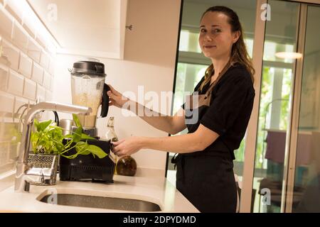 Jeune femme attrayante debout devant le blender dans sa cuisine, cuisant des repas végétariens frais pour la famille. Jeune femme blonde cuisine dans le TH Banque D'Images