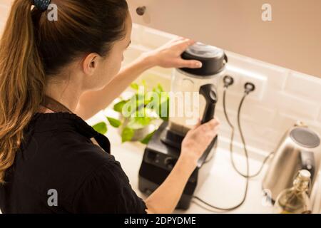 Jeune femme attrayante debout devant le blender dans sa cuisine, cuisant des repas végétariens frais pour la famille. Jeune femme blonde cuisine dans le TH Banque D'Images