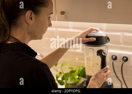 Jeune femme attrayante debout devant le blender dans sa cuisine, cuisant des repas végétariens frais pour la famille. Jeune femme blonde cuisine dans le TH Banque D'Images