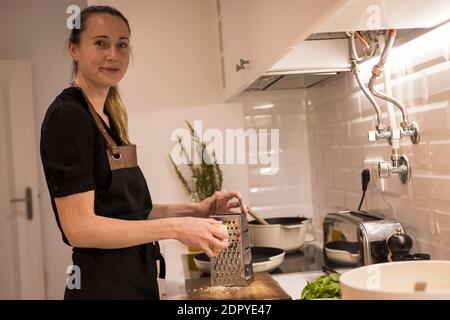 Jeune belle femme debout près du poêle et râper le fromage pour une recette saine de nourriture. Charmante femme norvégienne travaillant comme blogueur de nourriture et lif Banque D'Images