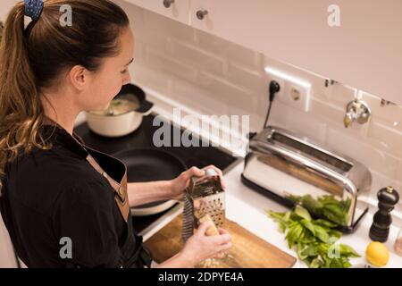 Jeune belle femme debout près du poêle et râper le fromage pour une recette saine de nourriture. Charmante femme norvégienne travaillant comme blogueur de nourriture et lif Banque D'Images