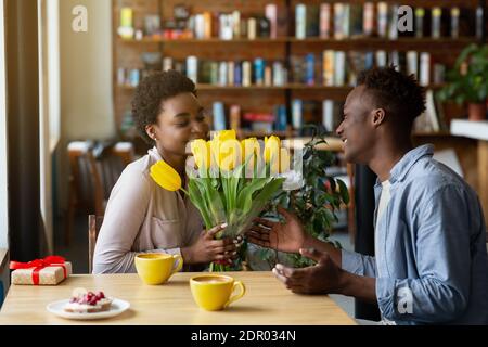 Beau gars noir donnant son bouquet de tulipes et sa petite amie Cadeau pour la Saint-Valentin au café Banque D'Images