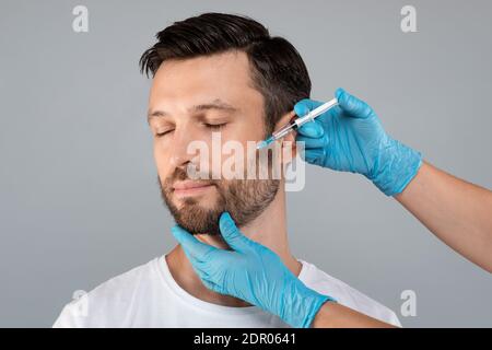 Beau homme d'âge moyen qui obtient la procédure anti-âge, fond gris Banque D'Images