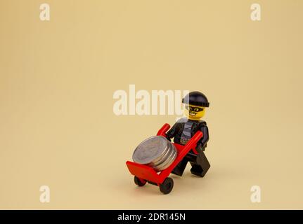 Ukraine, Kiev - 6 avril 2020 : un voleur LEGO à l'arme à feu prend des pièces sur une brouette. LEGO man Minifigure transporte de l'argent sur un chariot. Banque Banque D'Images