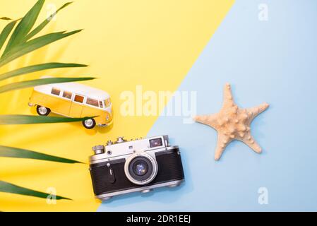 Étoiles de mer, appareil photo, feuilles de palmier et bus jouet sur fond jaune et bleu, concept de voyage Banque D'Images