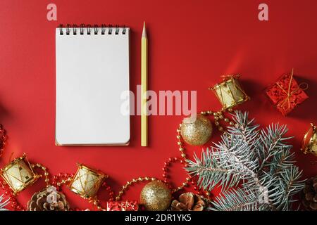 Bloc-notes et crayon pour écrire des voeux et des cadeaux pour le nouvel an et Noël autour des décorations d'arbre de Noël sur un fond rouge. Nouvel an moo Banque D'Images
