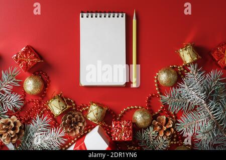 Bloc-notes et crayon pour écrire des voeux et des cadeaux pour le nouvel an et Noël autour des décorations d'arbre de Noël sur un fond rouge. Nouvel an moo Banque D'Images