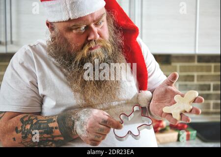 Image rognée d'un homme dans le chapeau du Père Noël tenant un moule à biscuit dans une main et un biscuit dans le autre Banque D'Images