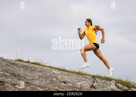 Vue latérale d'une femme de fitness qui fait de la course à haute intensité sur le flanc de la montagne par la mer Banque D'Images