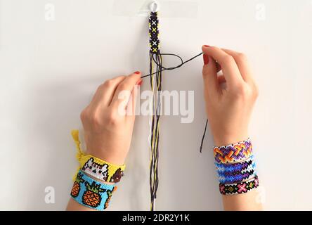 Processus de tissage du nœud pour le brielet d'amitié de bricolage. Mains de femmes avec beaucoup de bracelets faits main sur les poignets. Étape par étape. Banque D'Images