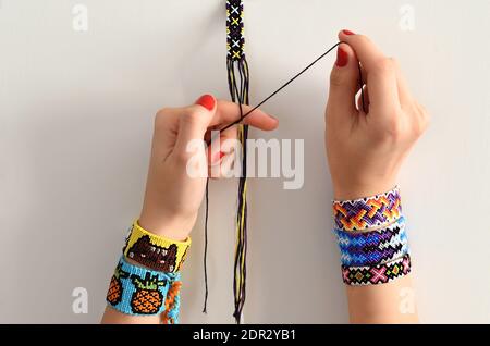 Processus de tissage du nœud pour le brielet d'amitié de bricolage. Mains de femmes avec beaucoup de bracelets faits main sur les poignets. Étape par étape. Banque D'Images