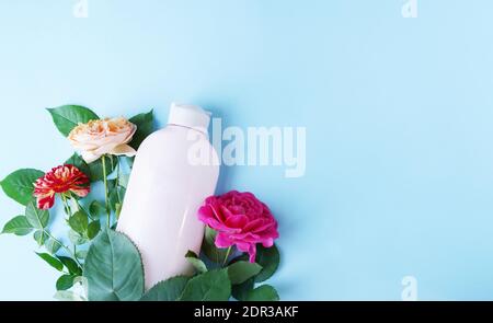 flacon de gel de shampooing sur fond bleu avec roses de fleurs roses, espace de copie, cosmétiques naturels biologiques, soins du corps Banque D'Images