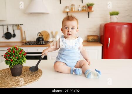 Mignon petit garçon de baie assis sur la table de cuisine et placage avec une grande cuillère Banque D'Images