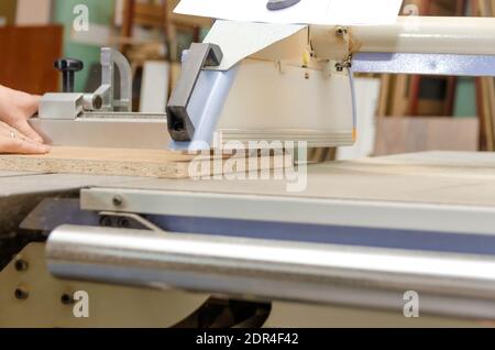 Un employé masculin se tient derrière une machine de découpe de format pour le traitement du bois. Machine à travailler le bois dans un atelier de menuisier Banque D'Images