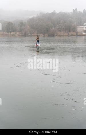 Homme debout sur un paddleboard debout sur un lac glacé Banque D'Images