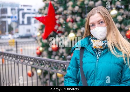 femme blonde dans un masque protecteur sur le fond d'un sapin de fête. Célébration de Noël et du nouvel an pendant la pandémie du coronavirus. Banque D'Images