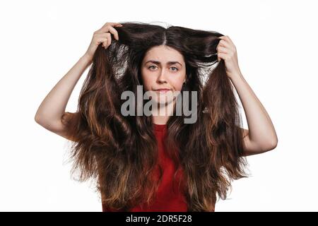 Le portrait d'une jeune femme mécontente montre ses cheveux épais et indisciplinés. Arrière-plan blanc. Le concept de coloration et de soin des cheveux. Banque D'Images