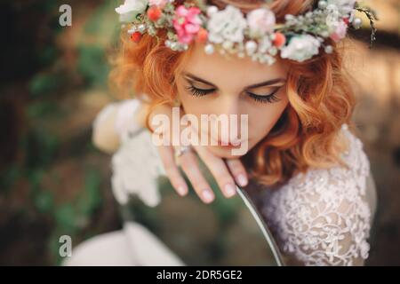 belle jeune mariée aux cheveux rouges dans la forêt avec une couronne florale sur sa tête et miroir . femme en robe blanche longue dehors le jour d'été. mariage Banque D'Images