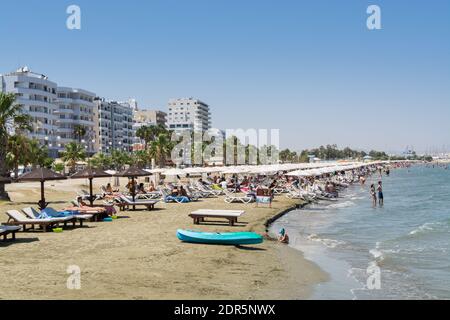 Beaucoup de touristes s'allonger sur des chaises longues sous les parasols À la plage de Larnaca Finikoudes de Chypre en été Banque D'Images