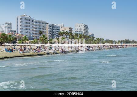 Beaucoup de touristes s'allonger sur des chaises longues sous les parasols À la plage de Larnaca Finikoudes de Chypre en été Banque D'Images