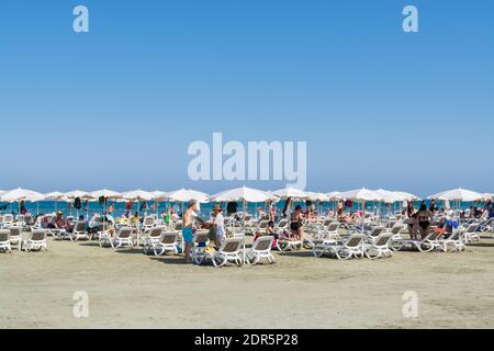 Beaucoup de touristes s'allonger sur des chaises longues sous les parasols À la plage de Larnaca Finikoudes de Chypre en été Banque D'Images