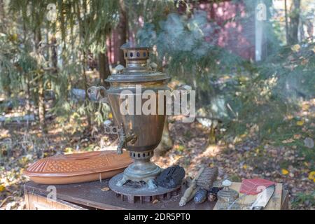 Samovar vintage, récipient en métal pour faire bouillir l'eau et faire du thé. L'eau est chauffée par un foyer intérieur, qui est un grand tuyau rempli de charbon de bois. Se dresse sur la véranda, sur fond de forêt. Photo de haute qualité Banque D'Images