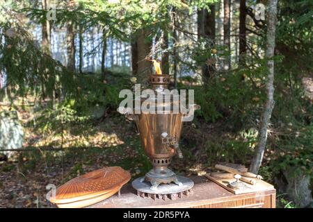 Samovar vintage, récipient en métal pour faire bouillir l'eau et faire du thé. L'eau est chauffée par un foyer intérieur, qui est un grand tuyau rempli de charbon de bois. Se dresse sur la véranda, sur fond de forêt. Photo de haute qualité Banque D'Images